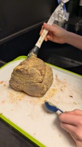 Eine Hand bestreicht das angebratene Filet mit Senf auf einem Brett mit grünem Rand
