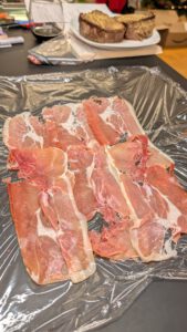 Dachziegelartig überlappende Parmaschinken-Scheiben auf Frischhaltefolie