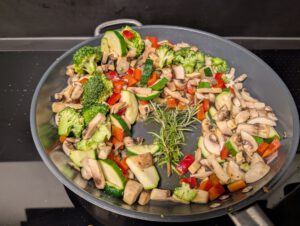 Brokkoli, Champignons, Zucchini und rote Paprika im Kreis am Pfannenrand, in der Mitte liegen Rosmarinzweige.