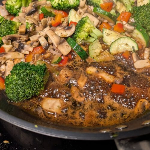 Pfanne voller Brokkoliröschen, Champignonscheiben, Zucchini und roter Paprika, unten blubbert dunkler Balsamico-Sirup.