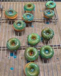 Grün und blau glasierte Mini-Donuts mit bunten Streuseln auf einem Kuchengitter mit Backpapier