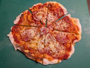 Gebackene Pizza in Stücke geschnitten auf einem grünen Brett