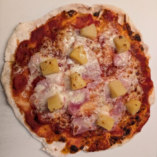 Gebackene Pizza mit Schinken, geschmolzenem Käse, Tomatensoße und Ananasstücken auf einer weißen Backunterlage