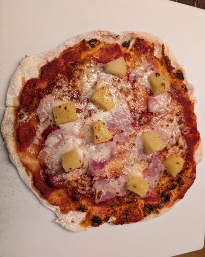 Gebackene Pizza mit Schinken, geschmolzenem Käse, Tomatensoße und Ananasstücken auf einer weißen Backunterlage