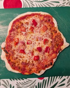 Frisch gebackene glutenfreie Pizza mit gebräuntem Käse, Tomatensoße und gewürfelter roter Paprika auf einem bemehlten grünen Schneidebrett