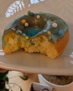 Ein glasierter Mini-Donut mit Streuseln und einem Bissen, der den weichen gelben Teig zeigt, auf einem weißen Teller