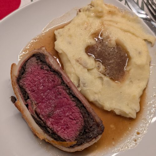 Cremiges Kartoffelpüree mit brauner Soße auf einem Teller neben einer Scheibe Beef Wellington