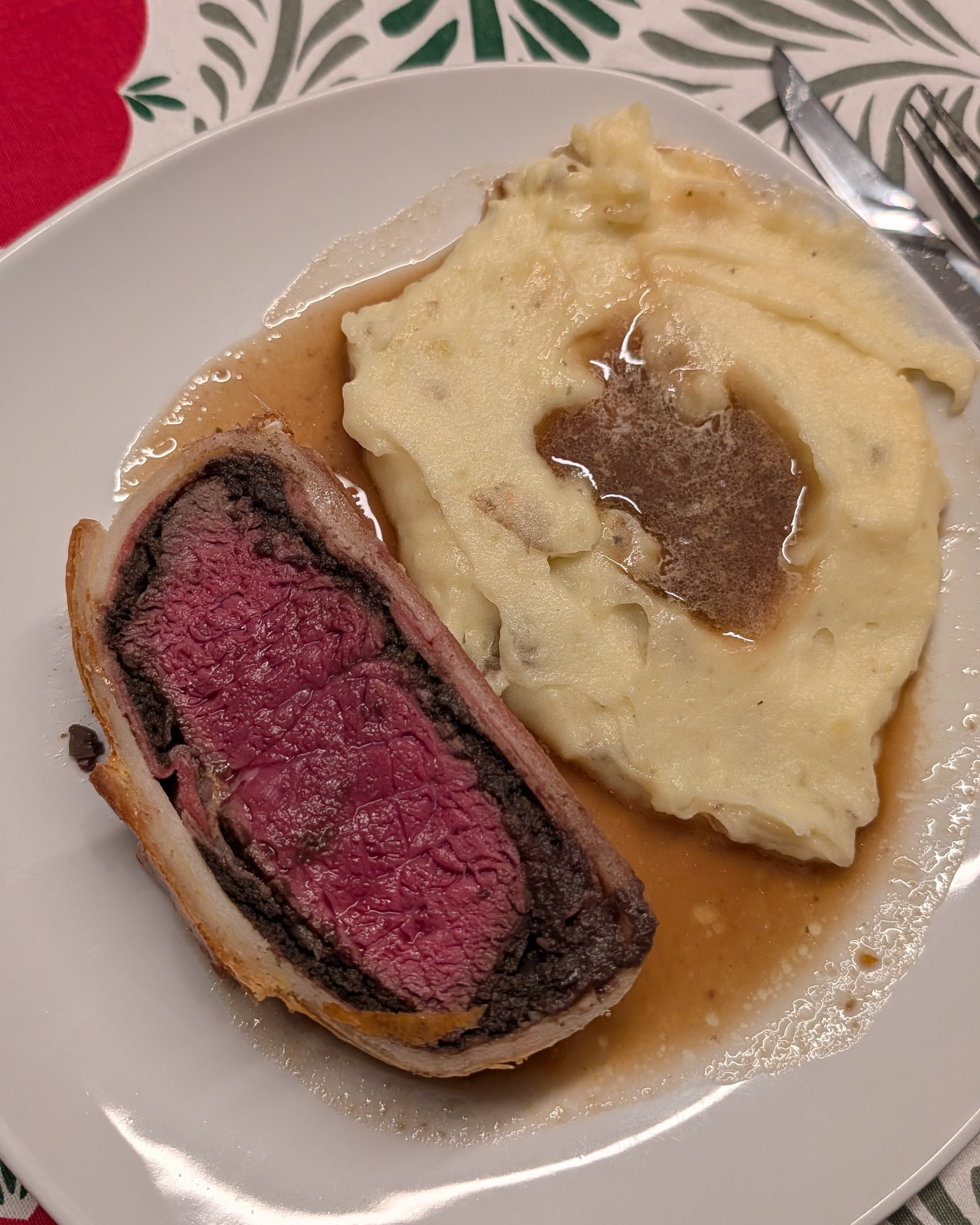 Cremiges Kartoffelpüree mit brauner Soße auf einem Teller neben einer Scheibe Beef Wellington