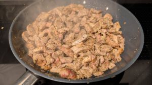 Gegarte Schweinefleischstücke in einer grauen Pfanne, es dampft