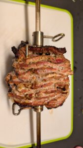 Herausgehobener Drehspieß mit den braunen, knusprigen Schichten des Fleischblocks auf einem weiß-grünen Schneidebrett