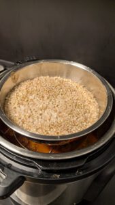 Instant Pot mit einer Edelstahlschüssel voll roher Buchweizengrütze auf dem Dreibein im Topf; die Fleischbällchen und die Soße darunter sind kaum zu erkennen