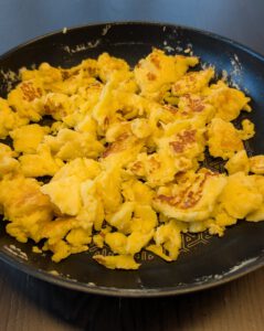 Goldgelbe, zerrissene Kaiserschmarrn-Stücke in einer dunklen Pfanne auf einem dunklen Holztisch