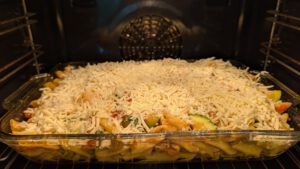 Ungebackener Penne-Auflauf in einer Glasform im Ofen, dick mit geriebenem Mozzarella bedeckt