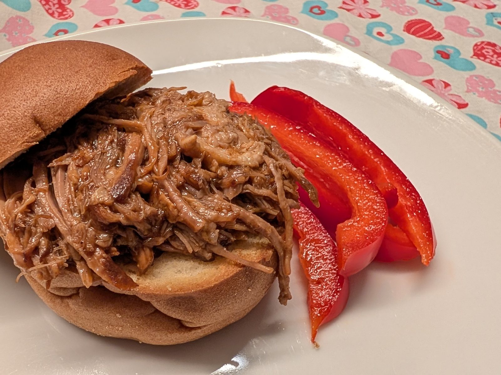 Glutenfreier Pulled-Pork-Burger auf einem weißen Teller mit roten Paprikastreifen