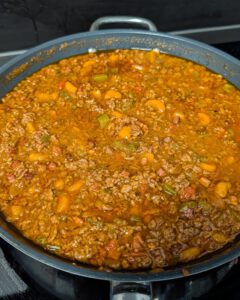 Ragù alla Bolognese köchelt in einer breiten Pfanne mit Rinderhack, Pancetta sowie Karotten- und Selleriestücken