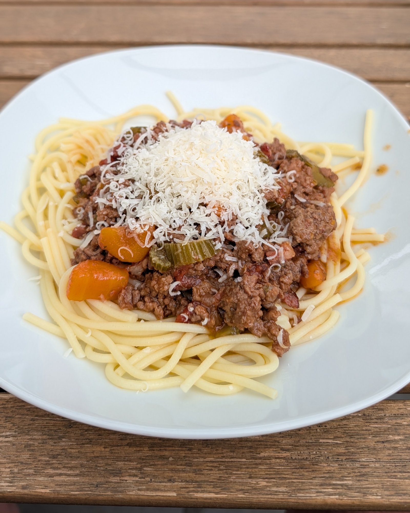 Teller mit Spaghetti, darauf Ragù alla Bolognese und ein Häufchen geriebener Käse, auf einem Holztisch
