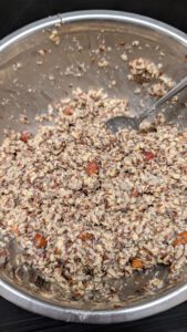 Dicker Saatenbrot-Teig mit einem Löffel in einer Stahlschüssel, Haferflocken, Samen, Nussstücke und graue Chiasamen sichtbar