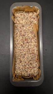 Saatenbrot-Teig glatt in eine mit Backpapier ausgelegte Kastenform gedrückt, von oben gesehen, bereit für die Ruhe über Nacht im Kühlschrank