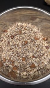 Trockene Mischung aus Haferflocken, Sonnenblumenkernen, Leinsamen und ganzen Nüssen in einer Edelstahlschüssel, bevor die Flüssigkeit dazukommt