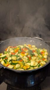 Gewürfelte Zucchini und rote, gelbe und grüne Paprika brutzeln dampfend in einer großen Pfanne auf dem Herd